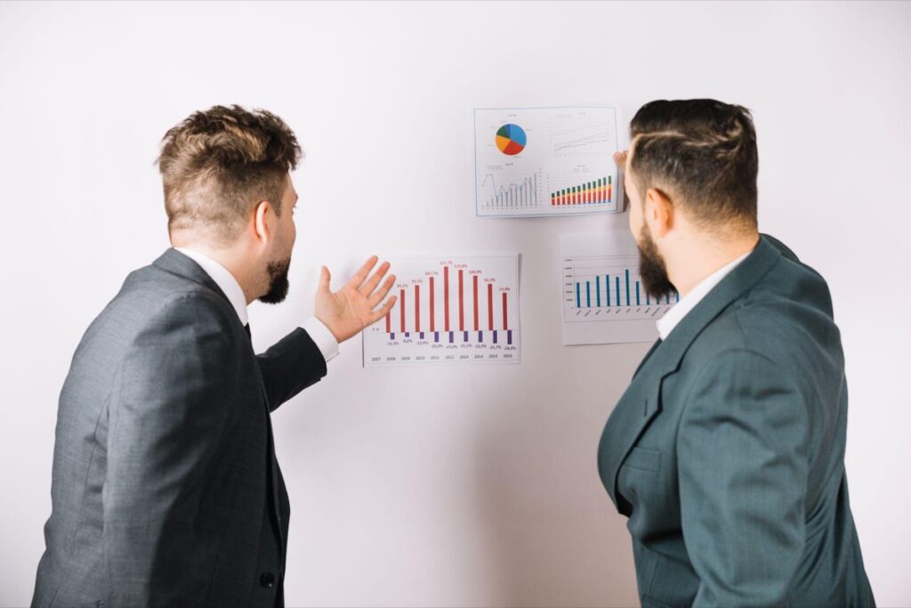 Two sales professionals reviewing performance charts on a wall