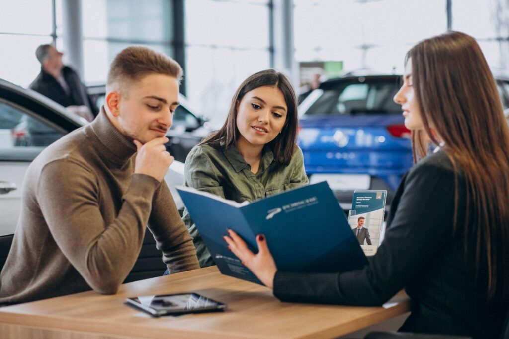 Two prospective buyers discuss vehicle ownership costs with a dealership representative